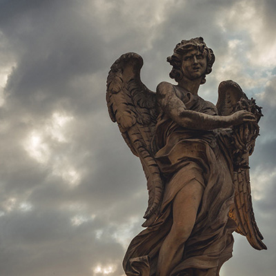 Angel sculpture agains grey cloudy sky.