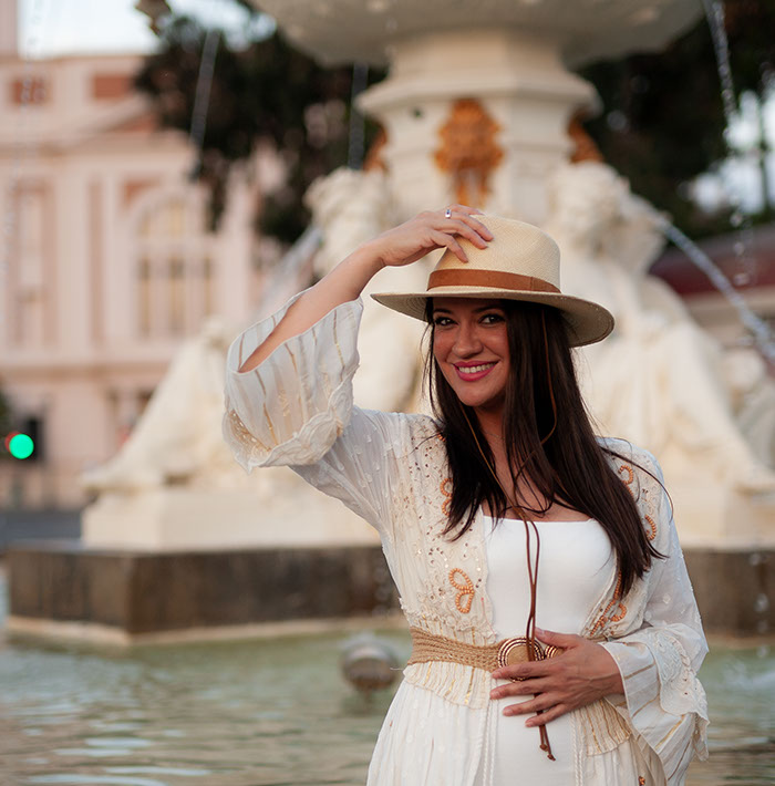 Girl in white dress in a hat next to the fountain.