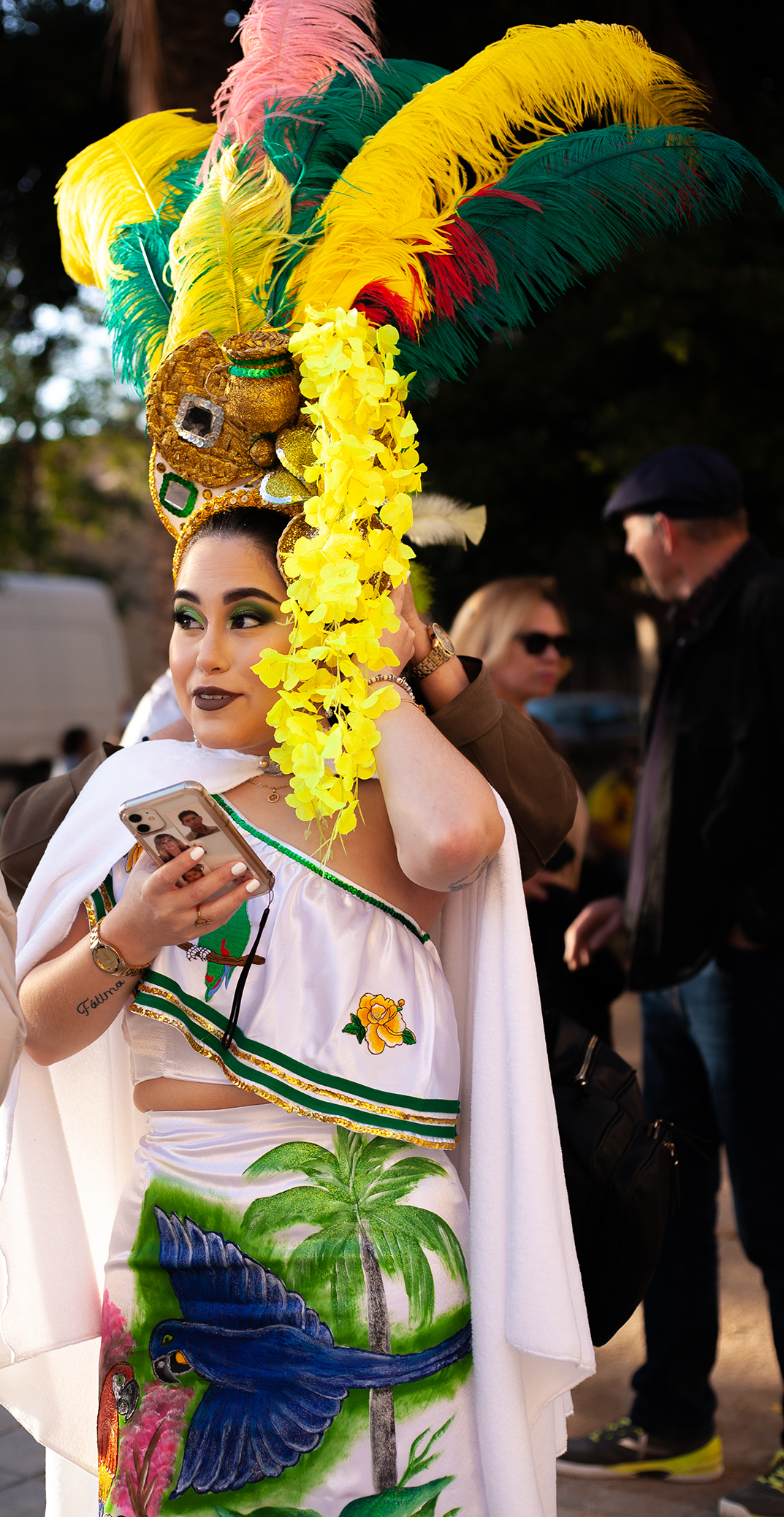 Girl in a white dress with paitings of parrots and palm tree on it, on her head big vivid yellow and green feathers