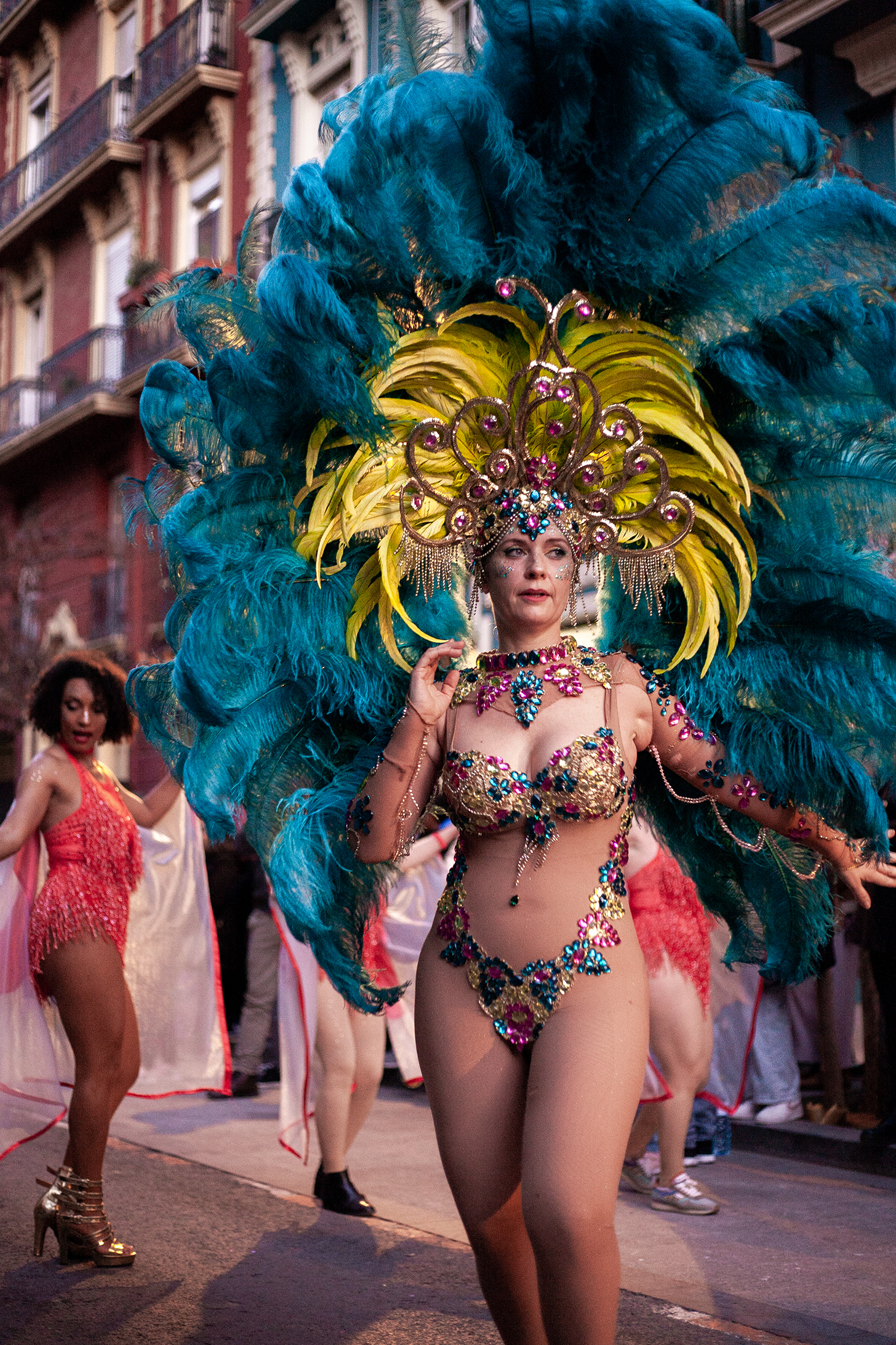 A woman dressed in naked style nylon with colorful stones as a lingerie. On her head enormous decoration from yellow feathers, and gigantic dark blue feathers