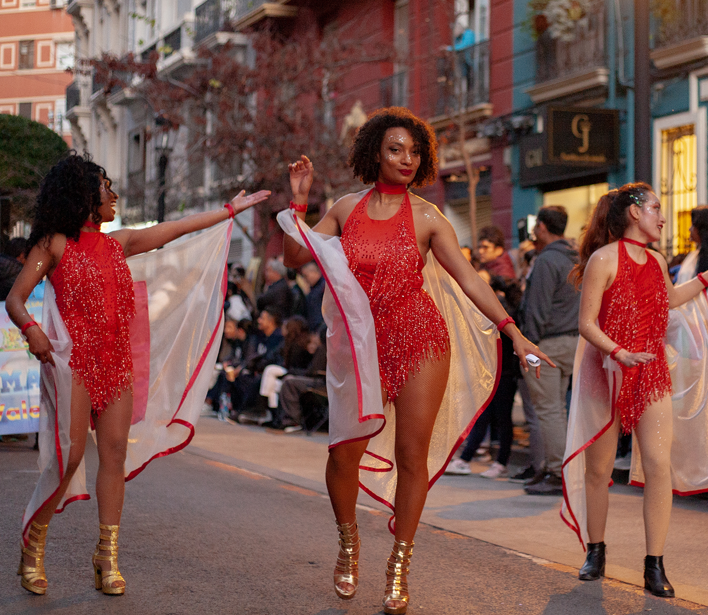 3 girls in a dancing formation walking the street, all dressed the same in sparking vivid red dresses, middle girl looking straight into camera and smiling sligthly