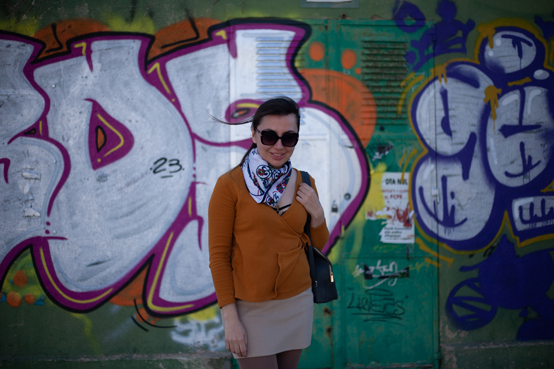 Girl in red coat, brown hair posing in garden with orange trees in background.