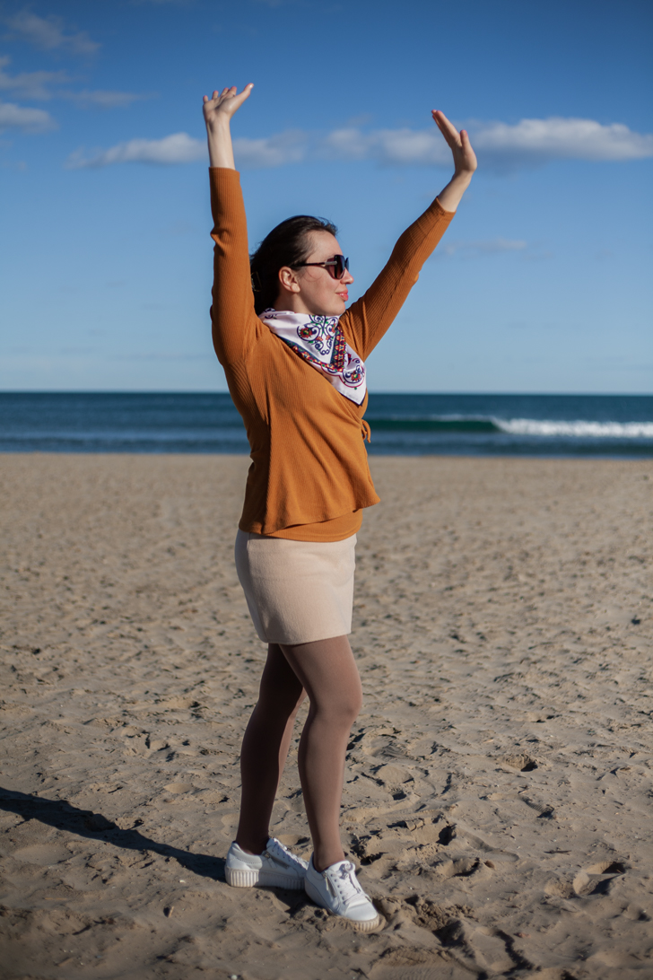 Girl in red coat, brown hair posing in garden with orange trees in background.